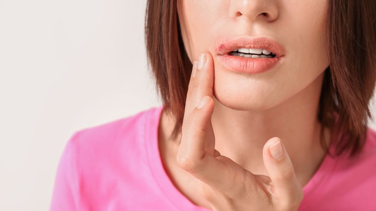 Egy nő az ajkát tapogatja, jelezve a herpesz vagy afta tüneteit.